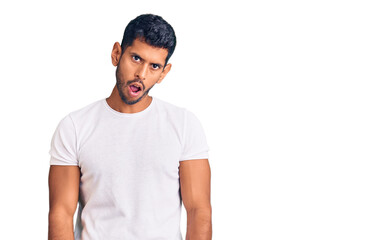 Young latin man wearing casual clothes in shock face, looking skeptical and sarcastic, surprised with open mouth