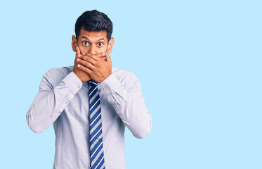 Young latin man wearing business clothes shocked covering mouth with hands for mistake. secret concept.