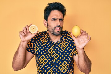 Handsome hispanic man with beard holding lemon clueless and confused expression. doubt concept.