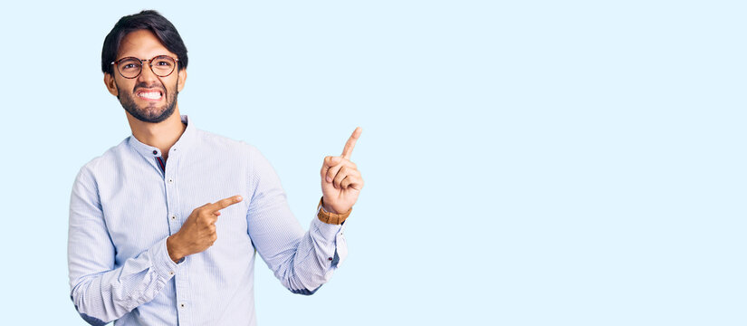 Handsome hispanic man wearing business shirt and glasses pointing aside worried and nervous with both hands, concerned and surprised expression