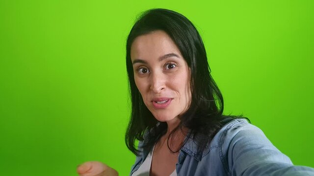 smiling woman posing on green screen background. Girl making a video call self portrait photo on smartphone. Chroma key. Female model showing positive face emotions

