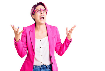 Obraz na płótnie Canvas Young beautiful woman with pink hair wearing business jacket and glasses crazy and mad shouting and yelling with aggressive expression and arms raised. frustration concept.