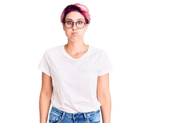 Young beautiful woman with pink hair wearing casual clothes and glasses puffing cheeks with funny face. mouth inflated with air, crazy expression.