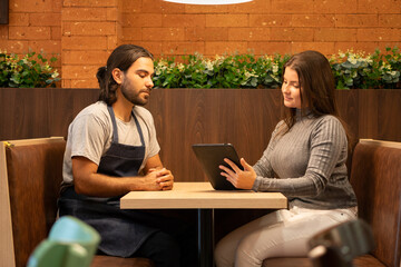 Serious latin female professional with tablet giving feedback to employee at meeting inside...