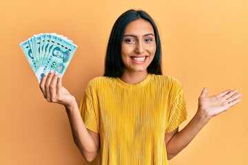 Young brunette woman holding 50 yuan chinese banknotes celebrating achievement with happy smile and winner expression with raised hand