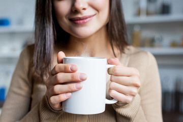 cropped view of pleased young woman holding cup of warm drink at home