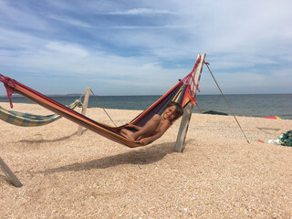 a tanned child smiles and lies in a hammock on the sea