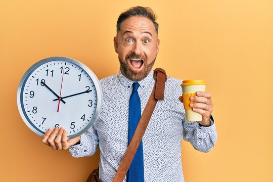 Handsome middle age business man drinking a cup of coffee and holding big clock celebrating crazy and amazed for success with open eyes screaming excited.
