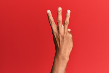 Hand of hispanic man over red isolated background counting number 3 showing three fingers
