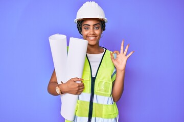Young african american woman with braids wearing safety helmet holding blueprints doing ok sign with fingers, smiling friendly gesturing excellent symbol