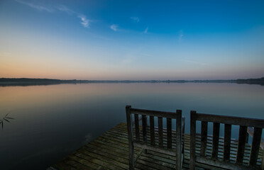 Lonely pier on a calm lake at sunrise with an old wooden chair