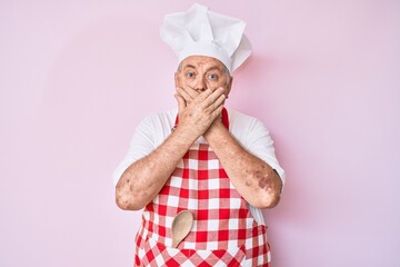 Senior grey-haired man wearing professional baker apron shocked covering mouth with hands for mistake. secret concept.