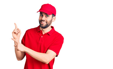 Young handsome man with beard wearing delivery uniform smiling and looking at the camera pointing with two hands and fingers to the side.