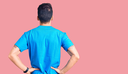 Young handsome man with beard wearing casual t-shirt standing backwards looking away with arms on...