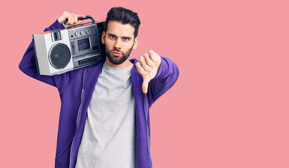Young handsome man with beard listening to music using vintage boombox with angry face, negative...