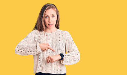 Young beautiful blonde woman wearing casual sweater in hurry pointing to watch time, impatience,...