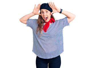 Young beautiful blonde woman wearing french beret and striped t-shirt smiling cheerful playing peek a boo with hands showing face. surprised and exited