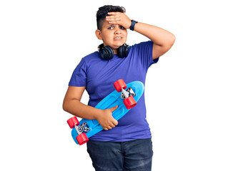 Little boy kid holding skate and wearing headphones stressed and frustrated with hand on head, surprised and angry face