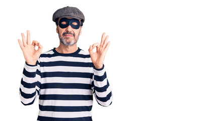 Middle age handsome man wearing burglar mask relax and smiling with eyes closed doing meditation gesture with fingers. yoga concept.