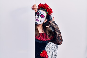 Young woman wearing day of the dead custome holding blank empty banner smiling doing phone gesture with hand and fingers like talking on the telephone. communicating concepts.