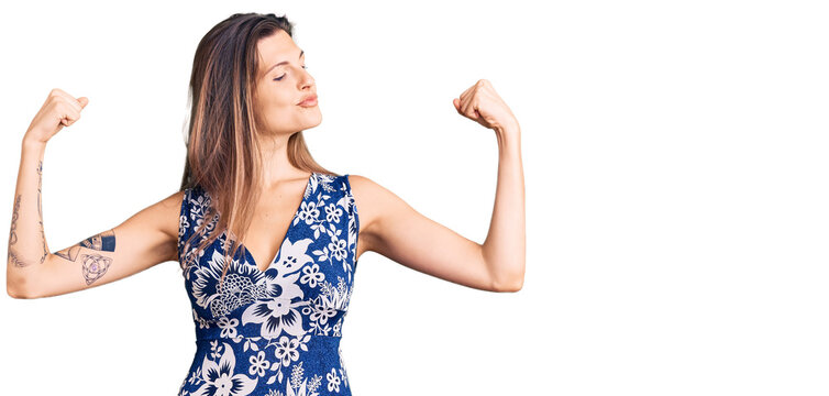 Beautiful caucasian woman wearing summer dress showing arms muscles smiling proud. fitness concept.