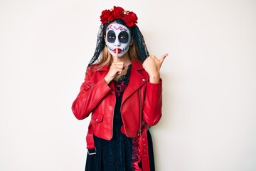 Woman wearing day of the dead costume over white asking to be quiet with finger on lips pointing with hand to the side. silence and secret concept.