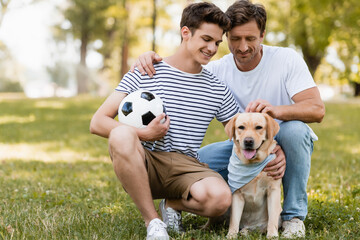 father sitting near teenager son with football cuddling golden retriever