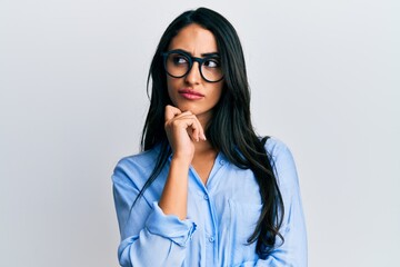 Beautiful hispanic woman wearing business clothes and glasses thinking concentrated about doubt with finger on chin and looking up wondering