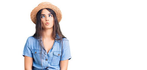 Brunette teenager girl wearing summer hat making fish face with lips, crazy and comical gesture. funny expression.