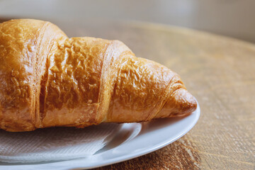 Fresh croissant on a white plate on a wooden table.