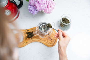 Making a perfect loose tea. Putting tea leaves by a teaspoon into a tea infuser in a glass teapot,...
