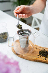 Making a perfect loose tea. Putting tea leaves by a teaspoon into a tea infuser in a glass teapot.