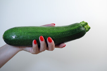 woman holding zucchini in manicured hand