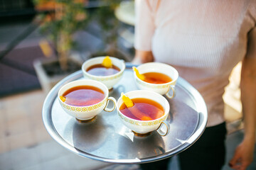 cuatro tazas de te con cascara de naranja servidas por una mujer
