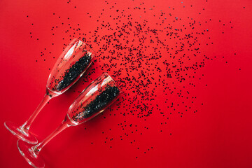 Champagne glasses with black confetti in the shape of stars on red background. Flat flat, top view, copy space. Holiday and celebration concept. Black Friday Sale background.