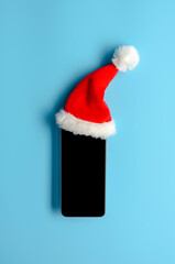 Obraz na płótnie Canvas Smartphone in christmas hat on blue background