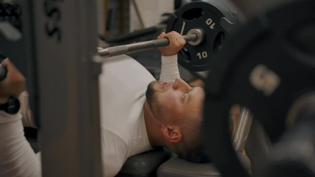 Powerful man does a bench press with a barbell. Muscular sports trainer conducts strength training in a modern gym.