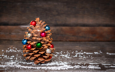 cone decorated with christmas ornament on dark wooden background with artificial snow