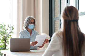 Old hr manager checking female job applicant cv resume at job interview meeting. Senior employer...