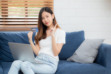 Young asian woman sitting thinking idea using credit card with laptop computer on couch, girl shopping online for buy and payment with notebook on sofa, finance and debit, lifestyle concept.