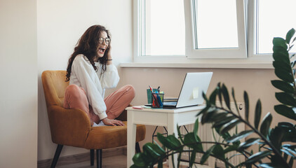 Excited caucasian woman screaming while talking with somebody on laptop and doing homework