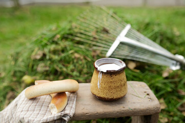 ceramic brown Cup with milk drink draining over the edge on old wooden stool and baking, green collected grass and forces on the background
