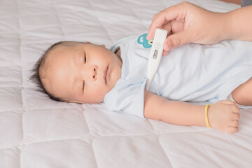 The mother measures the temperature of a sick newborn baby on the bed at home. Professional doctor checking thermometer of ill kid heat fever on armpit in hospital.