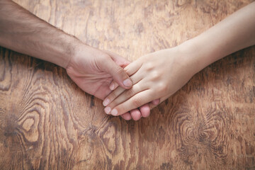 Young couple holding hands on wooden background.