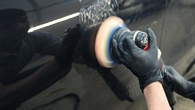 Car detailing - hands with orbital polisher in auto repair shop. Selective focus.