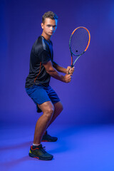 Fototapeta na wymiar Young tennis player in action against purple background