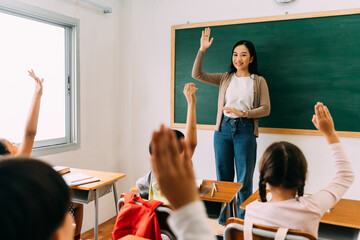 Asian school teacher with students raising hands. Young woman working in school with arm raised, school children putting their hands up to answer question, enthusiasm, eager, enjoyment. - 379274398