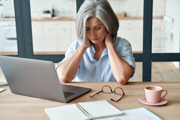Tired stressed old mature business woman suffering from neckpain working from home office sitting...