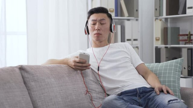 asian male record producer with headset and nodding slightly is listening to a demo on phone, feeling good about its melody.