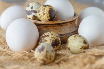 White raw chicken eggs and small quail eggs in a clay bowl on a burlap close-up. Chicken and quail eggs rustic background.